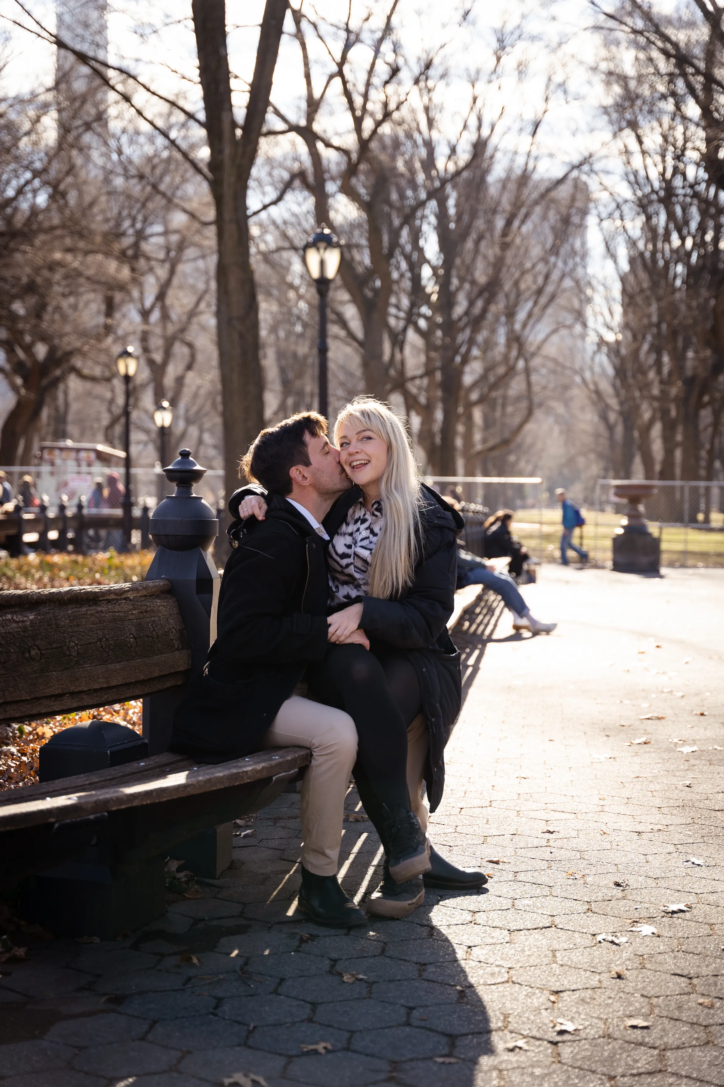 Sally laughing as Igor kisses her cheek on a park bench